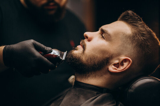 Handsome man cutting beard at a barber shop salon