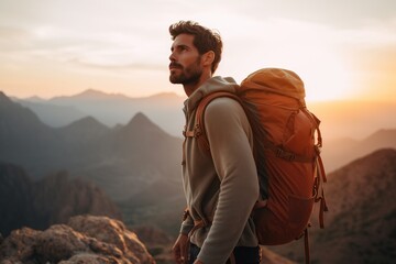 Handsome young man with backpack hiking in the mountains at sunset - obrazy, fototapety, plakaty