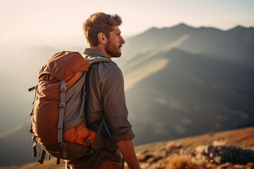 Handsome young man with backpack hiking in the mountains at sunset