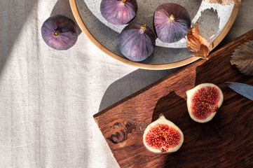 Cut fig on wooden board, fig fruits on plate, on beige linen tablecloth background. Lifestyle autumn food flat lay, healthy diet, vitamin and fiber source concept