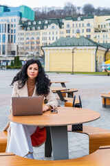 Woman online profession worker with laptop. Sits in a cafe on the street in a coat and looks straight into the frame