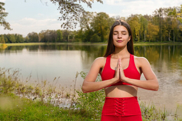 Naklejka na ściany i meble Portrait of attractive young girl in lotus pose feeling zen-like in city park, Outdoor yoga by the lake in a serene park