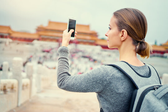 Enjoying vacation in China. Travel and technology. Young woman with smartphone taking photo at Forbidden City, Beijing.