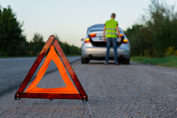 Unrecognizable sad driver in reflective vest. Male driver standing near broken car with open up...
