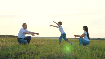 Active little boy runs between mother and father to hug parents in lush field