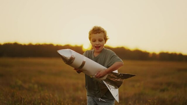 Joyful Child Boy Running In Meadow In Summer, Holding Toy Rocket In Hands, Slow Motion Portrait
