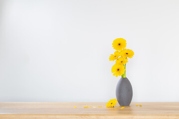yellow gerbera in  vase on wooden shelf