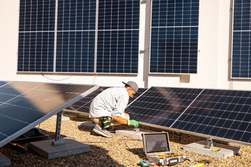 Man installing solar panels on the roof of his house, screwing cell on flat rooftop for self...