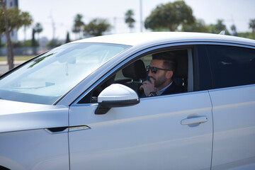 Fototapeta na wymiar Successful, attractive, young Hispanic man in jacket and sunglasses in thoughtful attitude inside his white luxury car. Concept, cars, luxury, success, businessman.