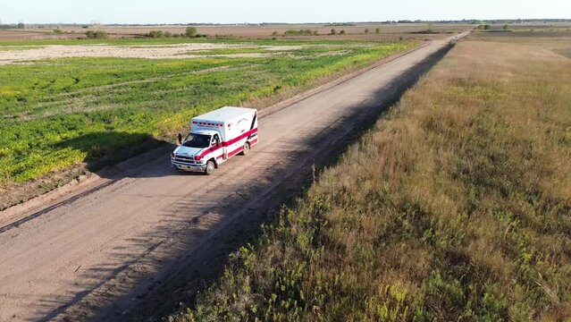 Drone footage of an ambulance car driving on an unpaved rural road in the fields