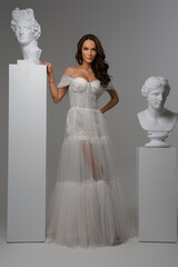 Beautiful model in resplendent white dress amidst Greek art sculptures in studio ambiance