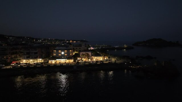 Il borgo di Acitrezza e i Faraglioni dei Ciclopi di notte. Sicilia, Italia. Vista aerea notturana della costa siciliana di Acitrezza.