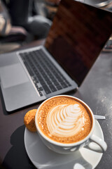 A cup Capuchino coffee. The table in the coworking space of the coffee shop. A cup of coffee on the veranda on a sunny day. Coffee break at the cafe. Close-up