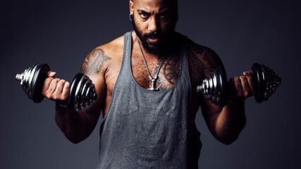 Black man with defiant attitude looks at camera holding two dumbbells in a studio shot