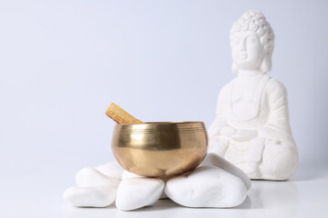 Bowl on stones and Buddha statue on white background, close up