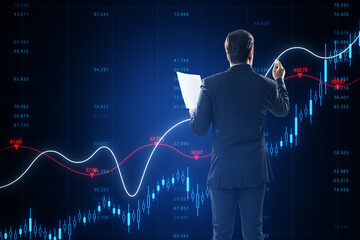 Back view of attractive young businessman holding document and using growing blue forex chart and index on blurry background. Trade and financial growth concept.