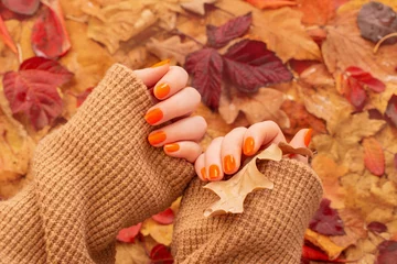 Poster female hands with orange manicure   on  background of autumn leaves © Maya Kruchancova