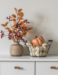 Autumn decor on the dresser in the living room - a bouquet of autumn leaves and berries and a...