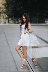 Photograph, portrait of a beautiful young brunette girl with curly hair, Armenian woman in a white dress in a park on the street outdoors.