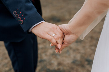 The bride and groom hold hands with gold rings on their fingers while walking outdoors. Wedding photography, close-up portrait.