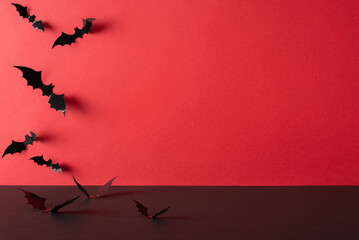 Halloween wall decor: Side view photo of a tabletop and eerie bat silhouettes against a red wall background, offering space for text or promotional content