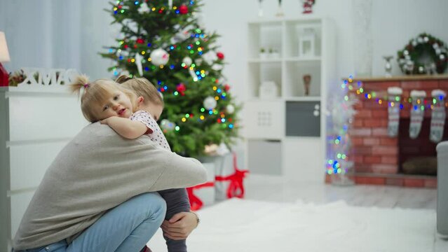 Mom very tenderly hugs her little daughter in a room full of Christmas decorations.