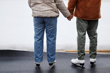 Back view of unrecognizable couple holding hands in ice skating rink, copy space