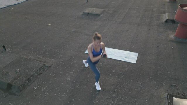 A fit woman does jumping lunges outdoors on a rooftop