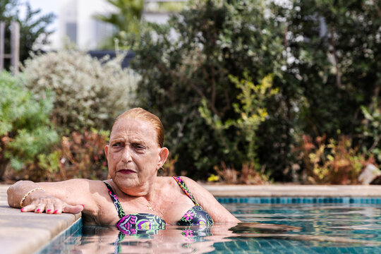 Photo of an older caucasian lady with a serious face while she is sitted inside the pool
