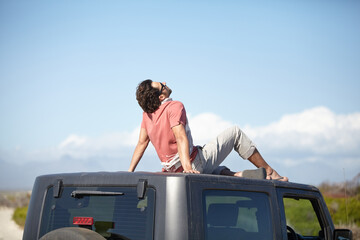 Travel, man and sitting on van roof for scenery, nature and fresh air on adventure or vacation in South Africa. Person, tourist or traveler on rooftop of car with sunglasses for view or road trip