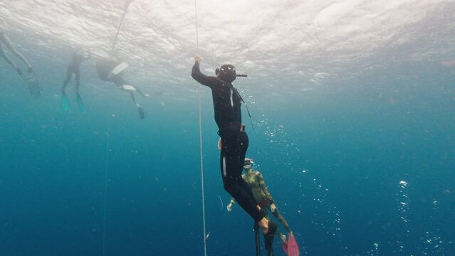 Male freediver trains in the sea and ascends along the rope with his buddy