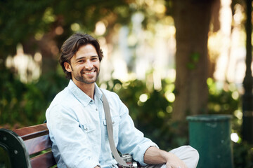 Travel, relax and portrait of a man on a park bench for a break, morning commute or summer. Smile,...