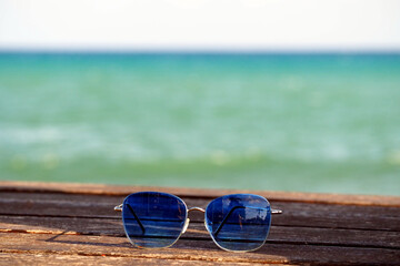 Fototapeta na wymiar Sunglasses with Blue Lenses on Wooden Bench by the Sea