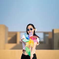 Asian woman posts and play Windmill Toy colourful rainbow colour on the building rooftop in sunset time.