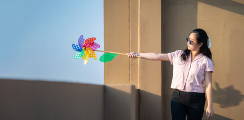 Asian woman posts and play Windmill Toy colourful rainbow colour on the building rooftop in sunset...