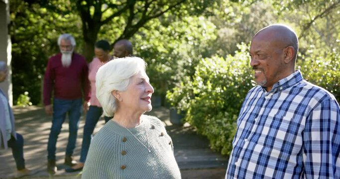 Happy diverse senior couple embracing in sunny garden, with friends, copy space, slow motion