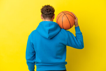 Young handsome caucasian man isolated on yellow background playing basketball in back position