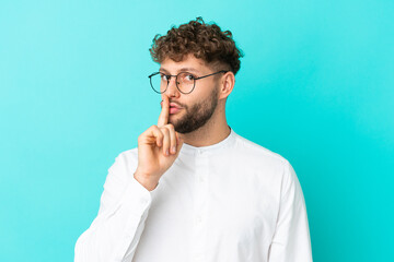 Young handsome caucasian man isolated on blue background With glasses and doing silence gesture