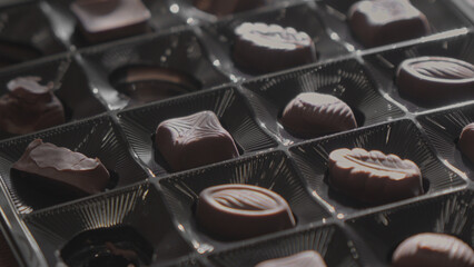 Chocolate candies of various shapes lie in box. Selective focus