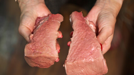 Pieces of raw pork meat in hands of woman who shows its quality.