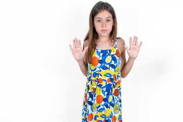 Serious Beautiful little kid girl wearing colorful dress pulls palms towards camera, makes stop...