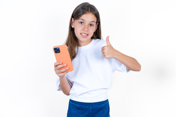 Portrait of Beautiful kid girl wearing white T-shirt using and texting with smartphone  happy with big smile doing ok sign, thumb up with fingers, excellent sign