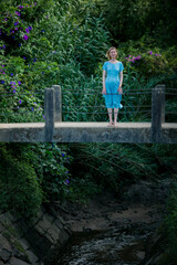 Standing on an ancient suspended bridge is a woman in a blue dress.