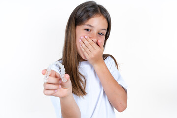 Happy Beautiful kid girl wearing white T-shirt holding and showing at camera an invisible aligner...