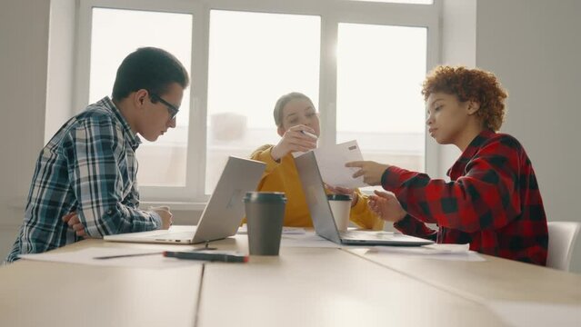 Team of office workers sit at table with documents and laptops and discuss work plan. Business planning. Process working together, analyzing, check data documentation and preparation report.