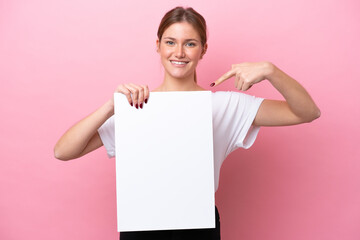 Young caucasian woman isolated on pink background holding an empty placard with happy expression...