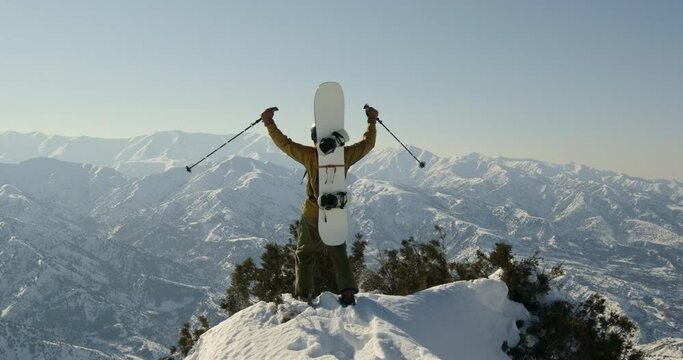 Snowboarder climbed mountain raises hands. Professional mountaineer snowboarder freerider in snowshoes climbed high slope conquered mountain raised hands enjoying view of snowy peaks of mountains