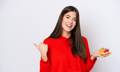 Young Brazilian woman holding a tartlet isolated on white background pointing to the side to present a product