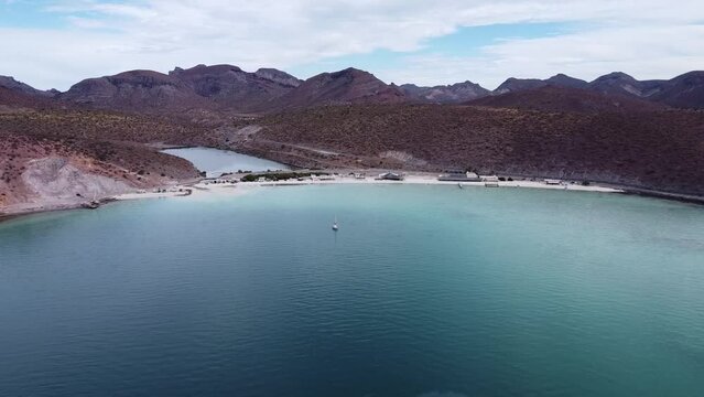 Aerial wide dolly shot of the beautiful Playa Pichilingue near Pichilingue port of La paz in Baja California Sur Mexico with blue sea with floating ships and rocky landscape with cloudy sky