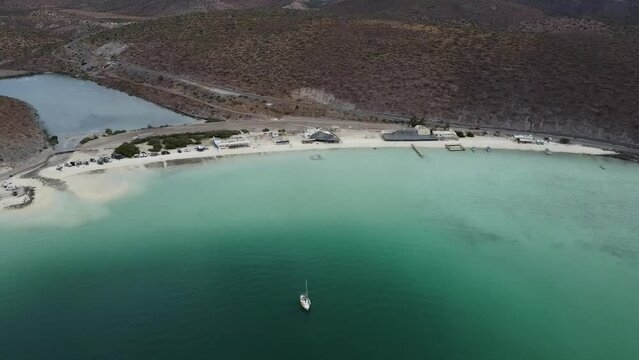 Aerial dolly backwards shot from the beautiful coast of Baja California Sur Mexico Pichilingue Beach near La Paz overlooking the wasteland or desert landscape and the calm sea with floating boats
